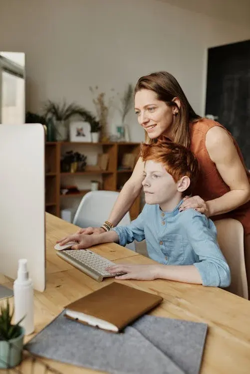 A woman and a child sitting together at a desk, looking at a computer screen