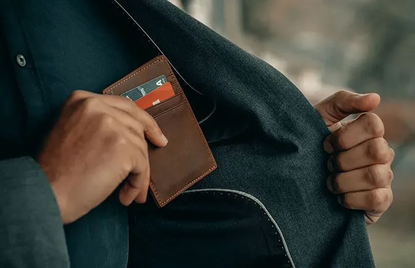 A person in a suit slipping a leather card wallet into an inside jacket pocket