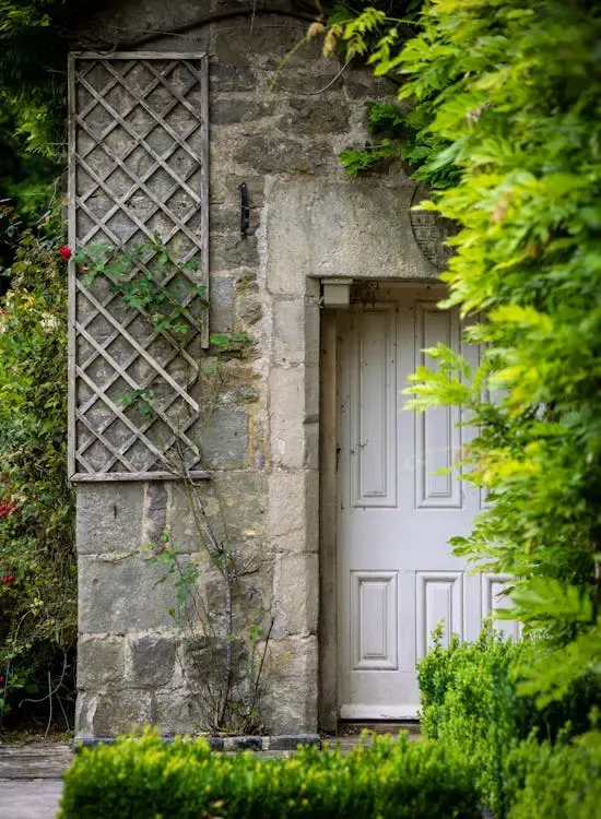 A white panelled front door set into a stone cottage wall, framed by greenery
