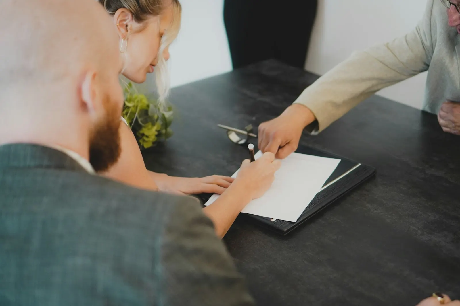Two people at a desk, one signing a document on a clipboard