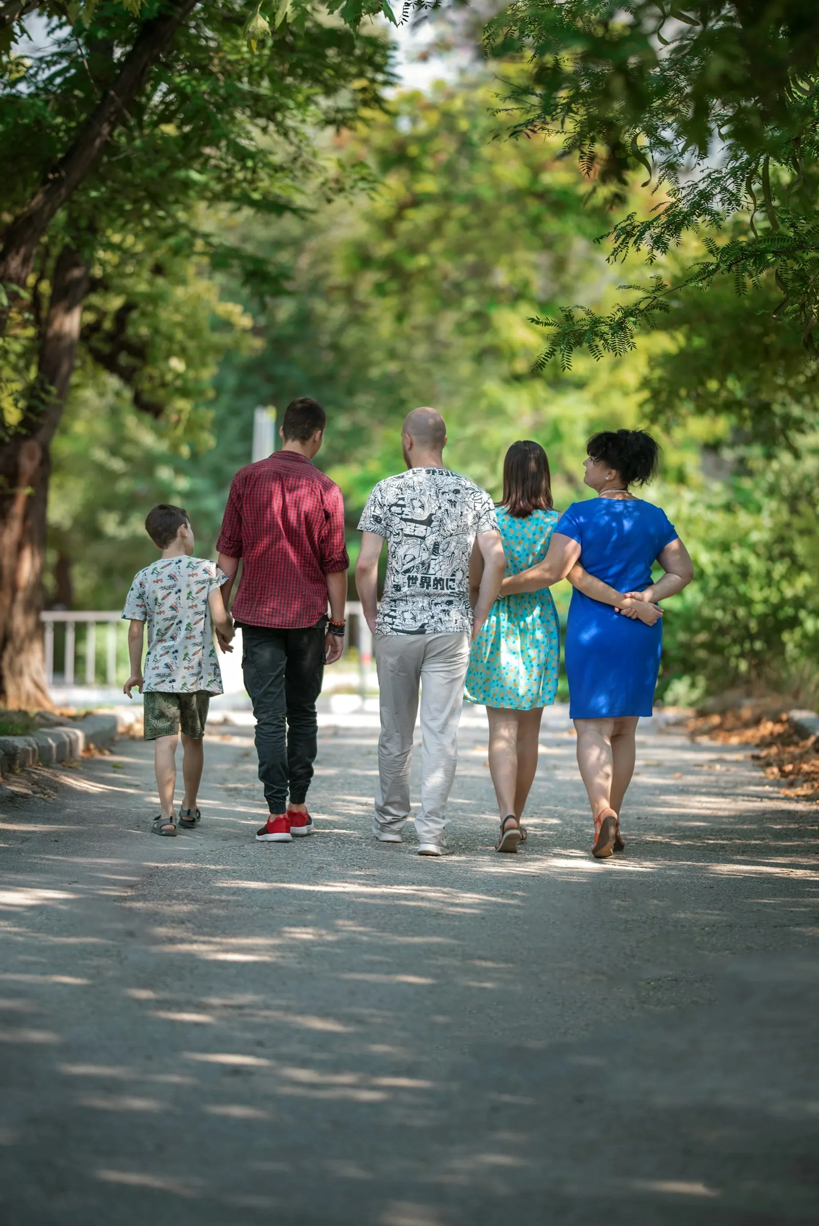 A family walking away down a tree-lined path, a child holding an adult's hand
